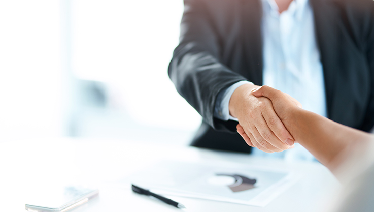 In a bright office, two individuals shake hands. 